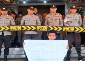 DEMO TUNGGAL: Seorang aktivis membentangkan poster dengan pengawalan ketat aparat kepolisian di depan teras kantor Bupati Sumenep, Selasa, 1 Agustus 2023. (Istimewa/Lingkarjateng.id)