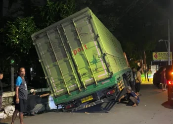 Truk bermuatan 37 ton terperosok ke selokan di Puri Kembangan, Jakarta Barat, evakuasi terkendala kabel listrik dan muatan keramik berat.